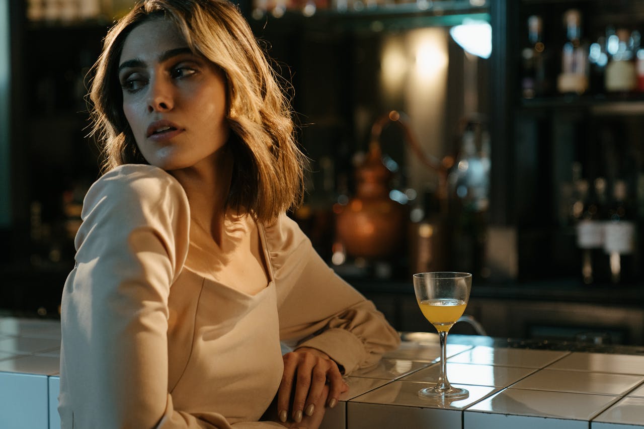 Sophisticated woman sitting at a bar counter with a cocktail, in a glamorous setting.