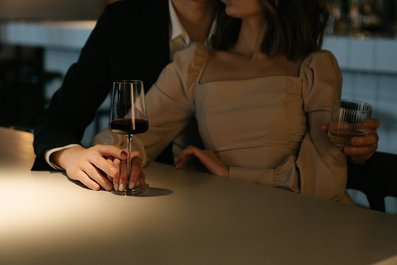 Intimate scene of a couple holding hands with drinks at a modern bar in soft lighting.